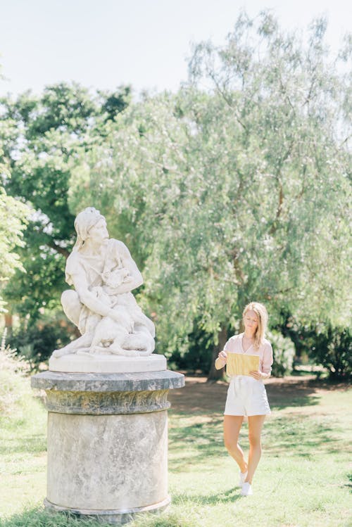 Женщина в белом платье стоит возле статуи