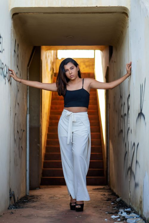 Free Woman in white pants and black crop top posing confidently in a graffiti-filled alleyway. Stock Photo