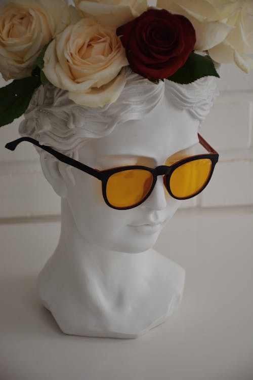 Free From above of trendy sunglasses on ornamental stone female bust decorated with blossoming flowers on white background Stock Photo