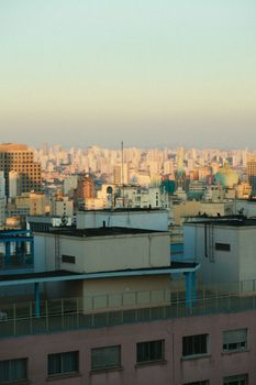 在白天，万里无云的天空下，城市街道上破旧公寓的屋顶与现代摩天大楼形成背景