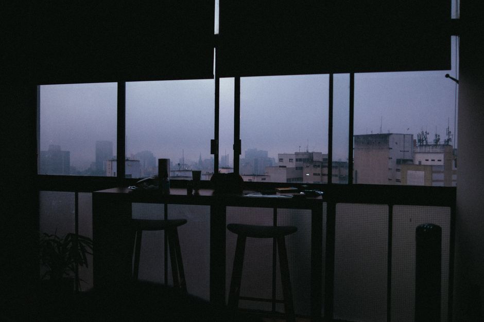 Interior of contemporary dark room with table and chairs and big windows overlooking city buildings in foggy weather in daytime