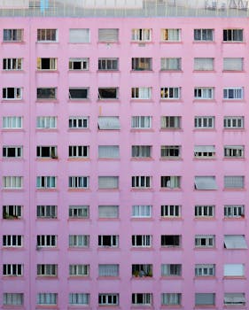Facade of contemporary apartment house with rectangle windows located in rows and pink wall in city street in daylight outside