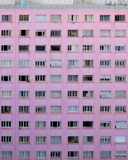 Facade of contemporary apartment house with rectangle windows located in rows and pink wall in city street in daylight outside