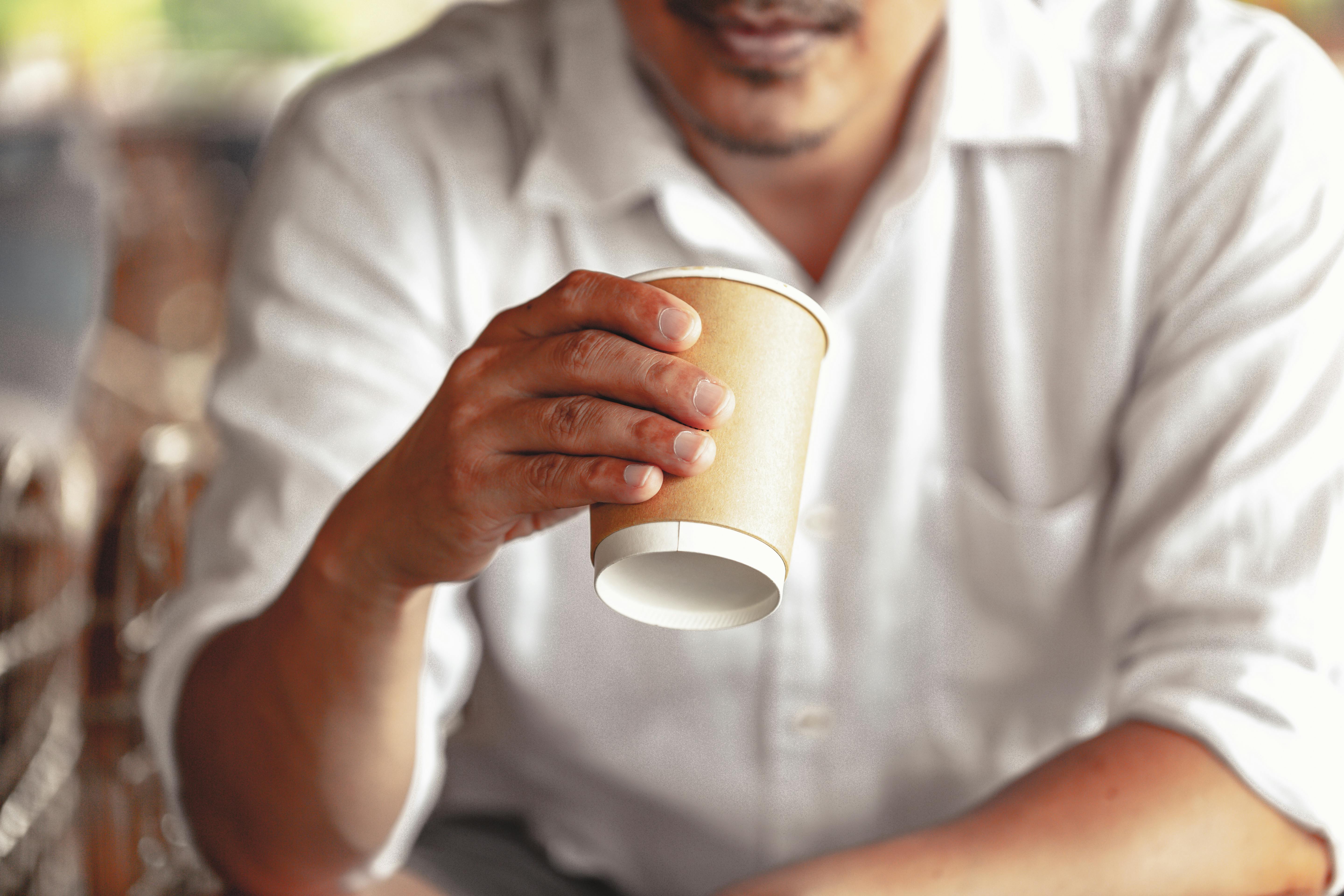 Close-up of a man holding a disposable coffee cup, wearing a white shirt.