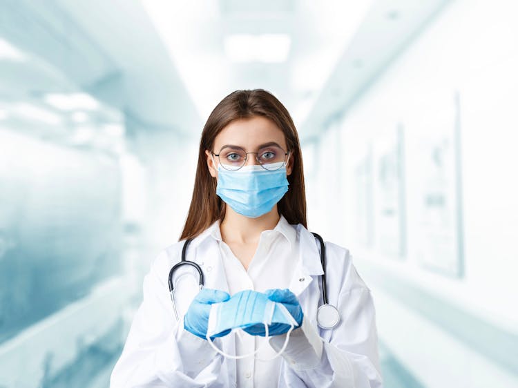 A Young Woman In White Coat Wearing And Holding  Face Masks