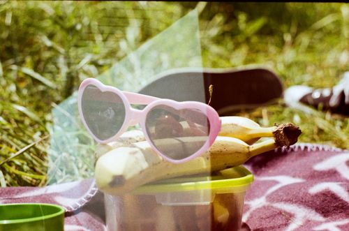 Free From above of modern sunglasses with ripe bananas on plastic container with food on textile on grass meadow Stock Photo