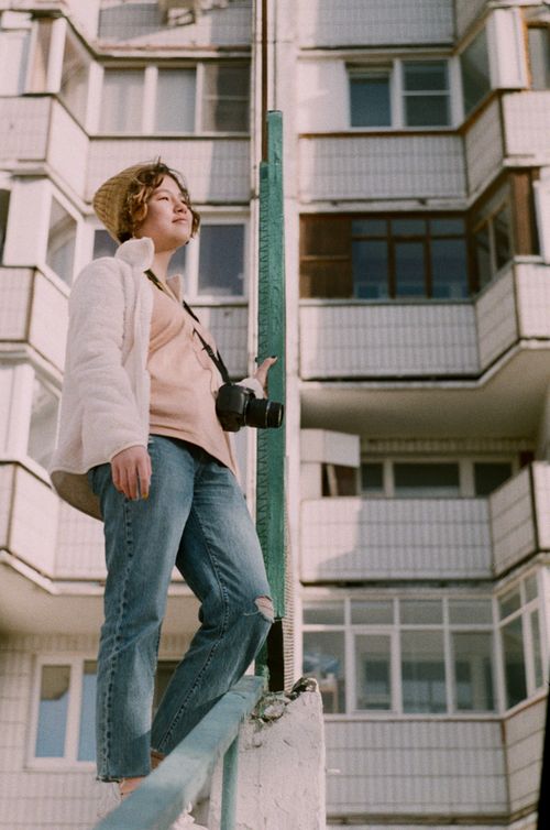 Free From below side view of young content female with photo camera looking away near residential multistory house Stock Photo
