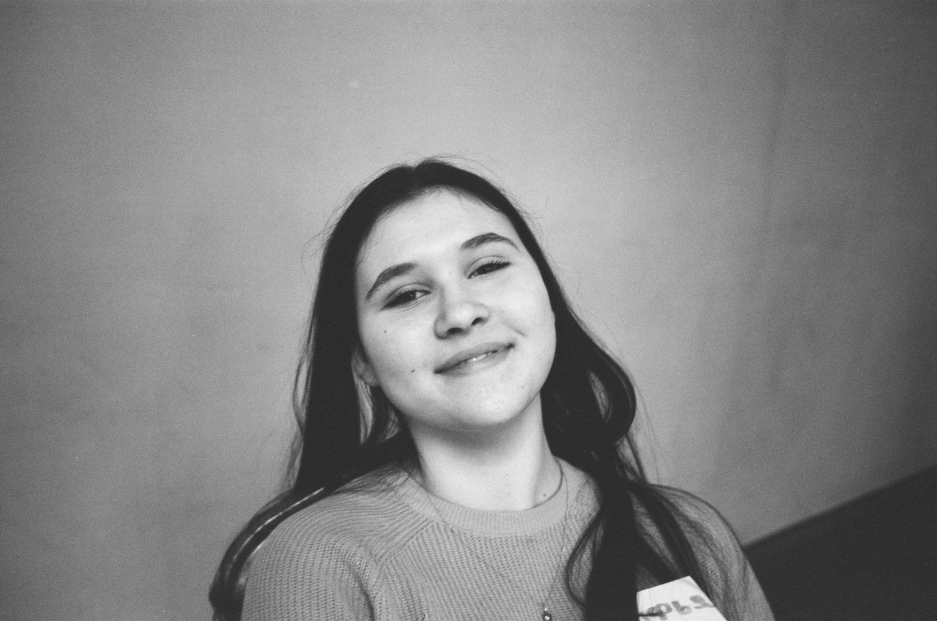 Black and white from above of cheerful female teenager in chain looking at camera near wall