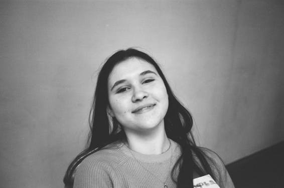 Black and white from above of cheerful female teenager in chain looking at camera near wall