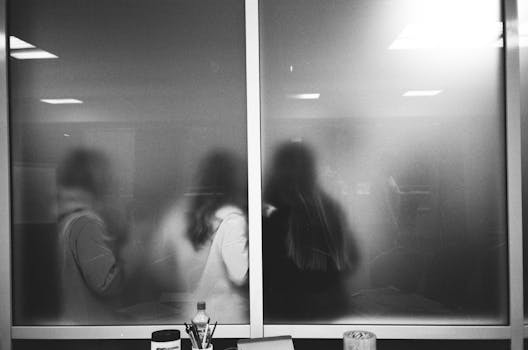 Black and white of office supplies near window with back view of anonymous women under shiny lamps