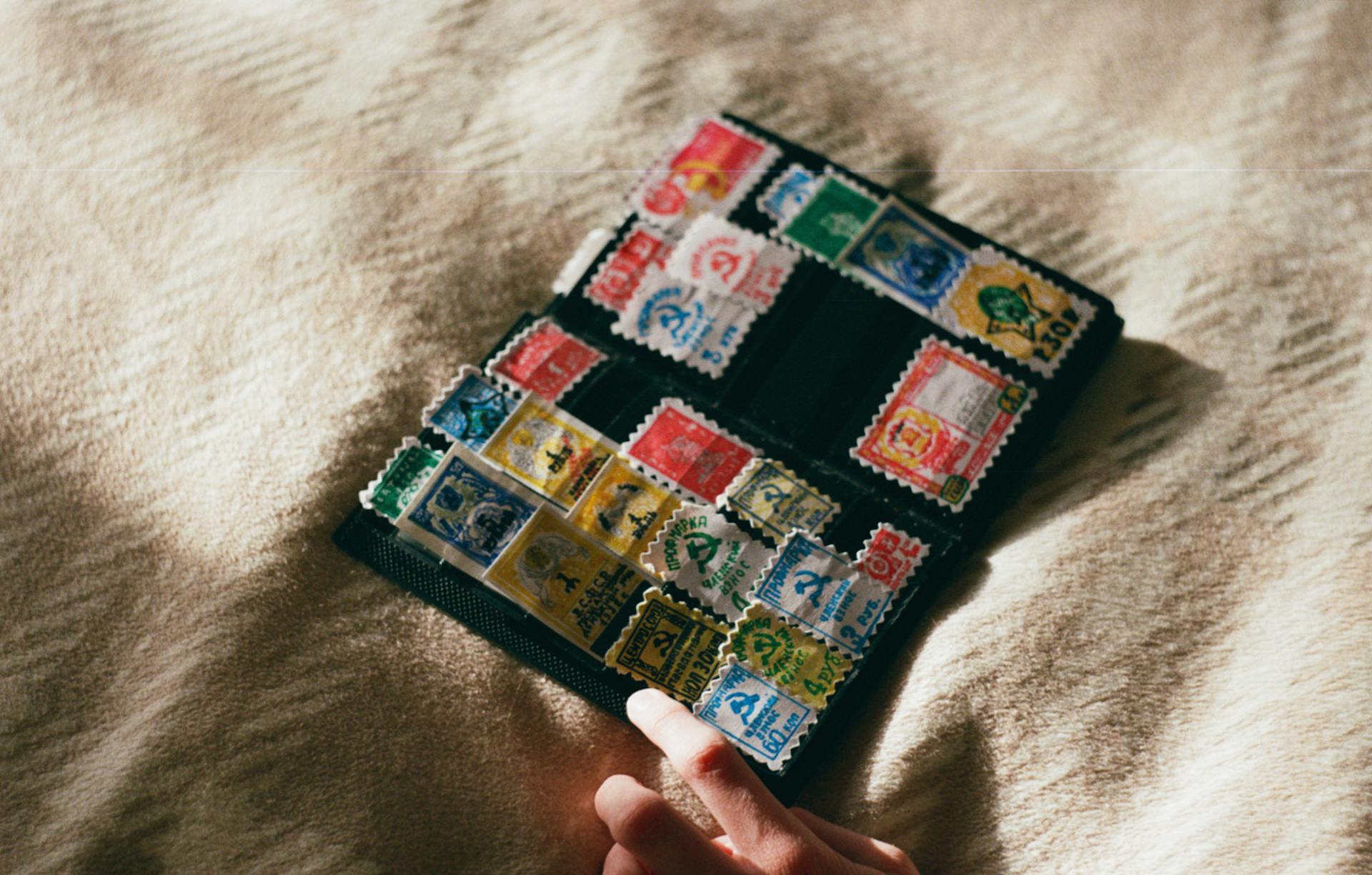 From above of crop unrecognizable person with collection of vintage stamps with illustrations on woolen textile