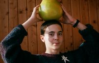 Adolescent with ripe pomelo on head in house