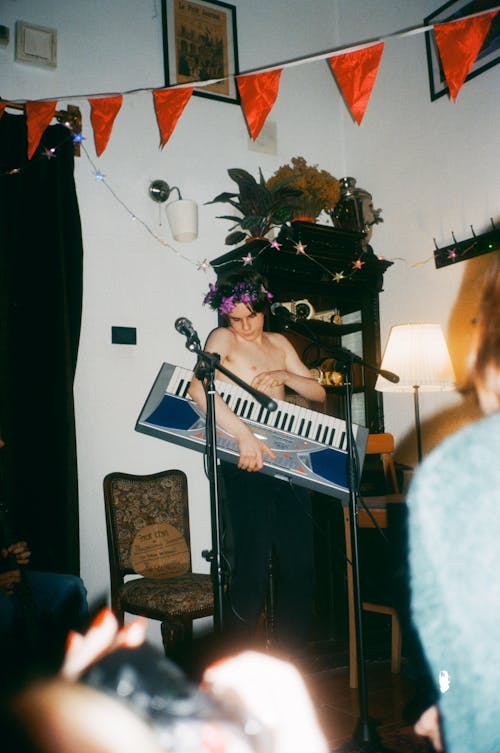 Музыкант с синтезатором в комнате с гирляндой возле анонимных друзей