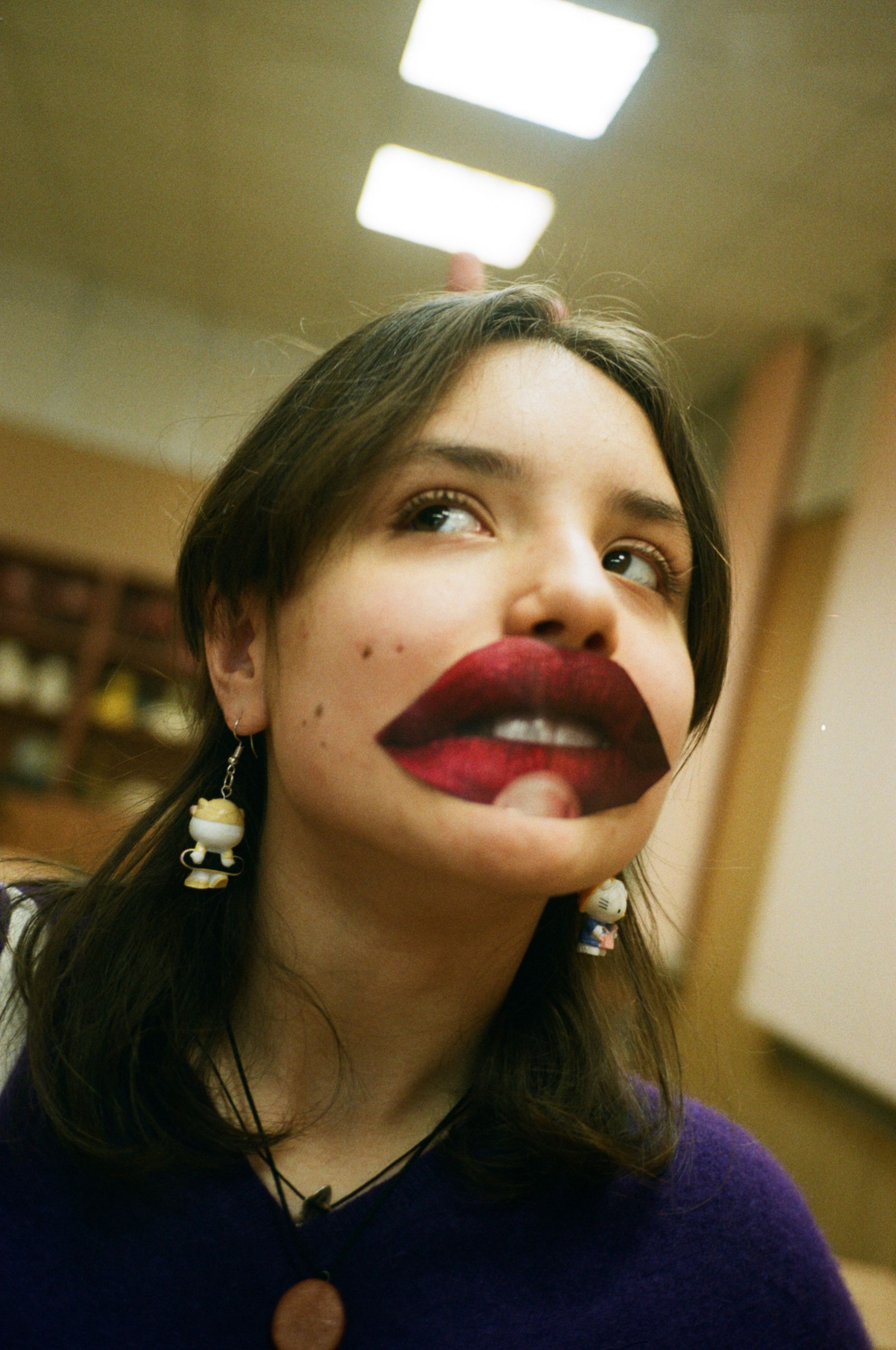 Funny adolescent in earrings with colorful decorative lips looking away under ceiling with glowing lamps