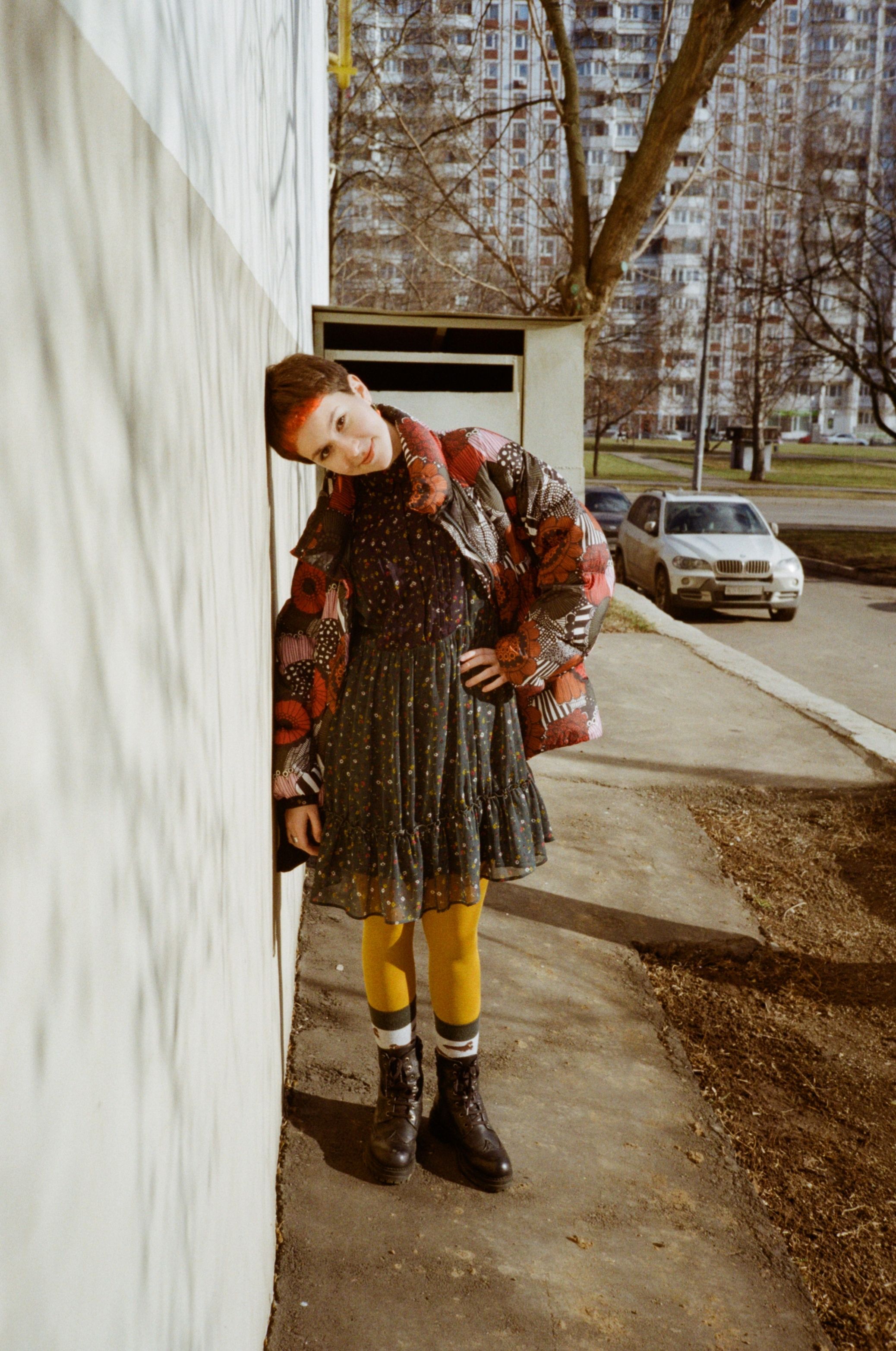 Full body of young informal female with short hair in trendy warm outfit standing on shabby sidewalk with hand on waist and looking at camera