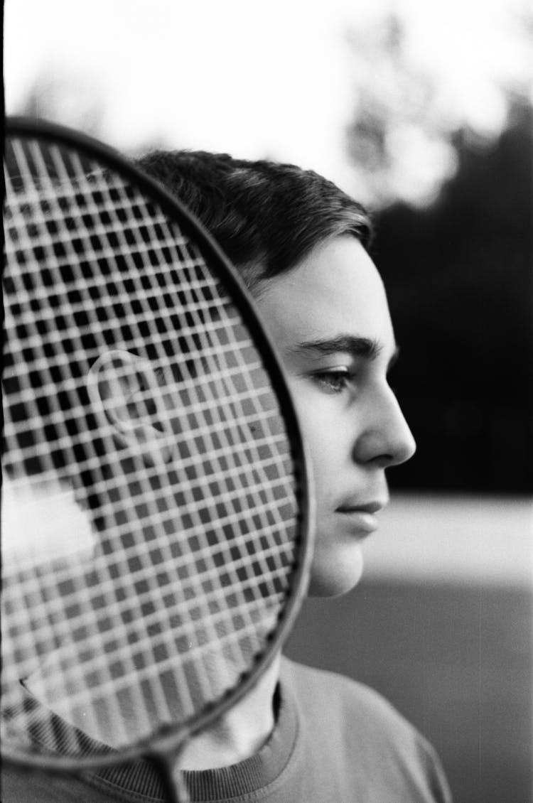 Pensive Teen Boy With Badminton Racket On Court