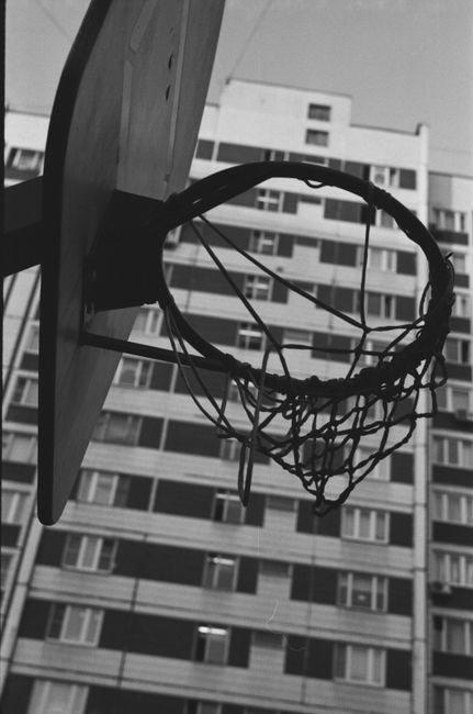 From below of black and white basketball hoop hanging on sports ground in city park near residential building