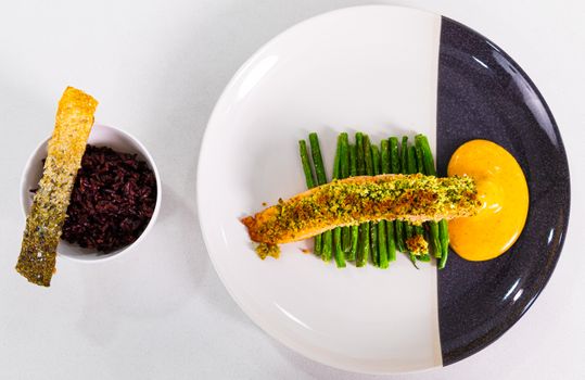 Delicious herb-crusted salmon with green beans, black rice, and sauce in a stylish presentation.