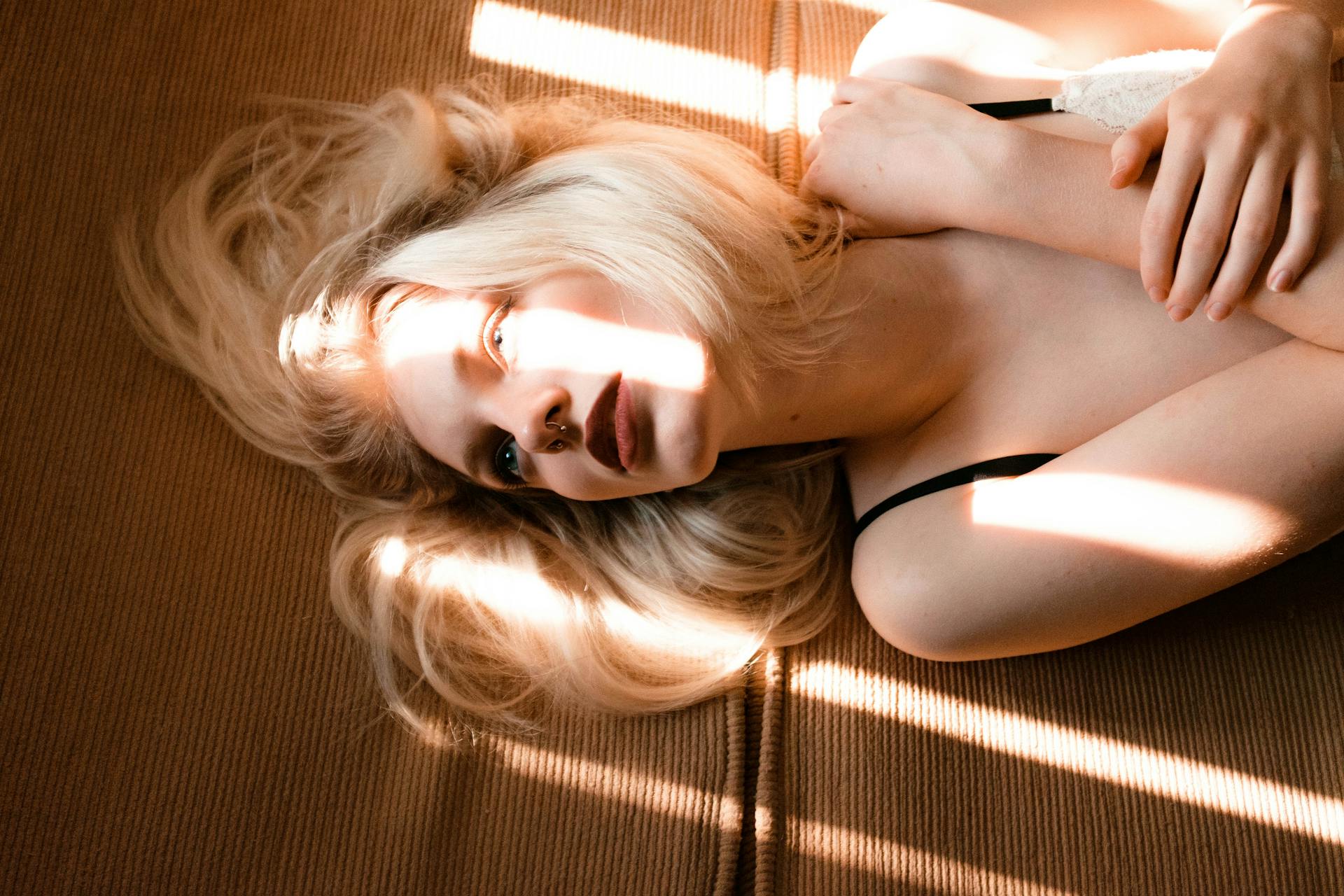 Blonde woman with septum piercing lying in sunlight, expressing tranquility and introspection.