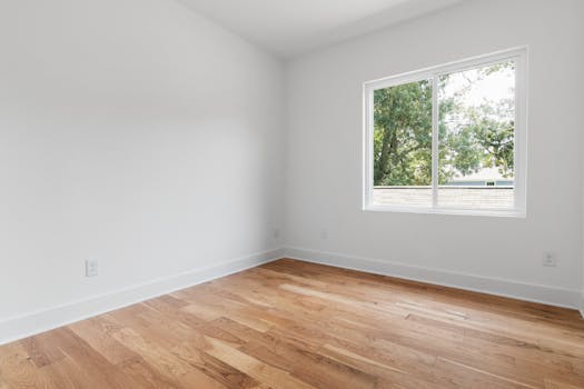 A clean empty room with wooden flooring and a window overlooking trees