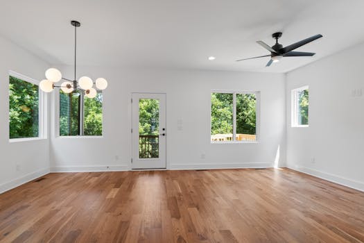 Spacious modern room with hardwood floors, large windows, and stylish lighting.