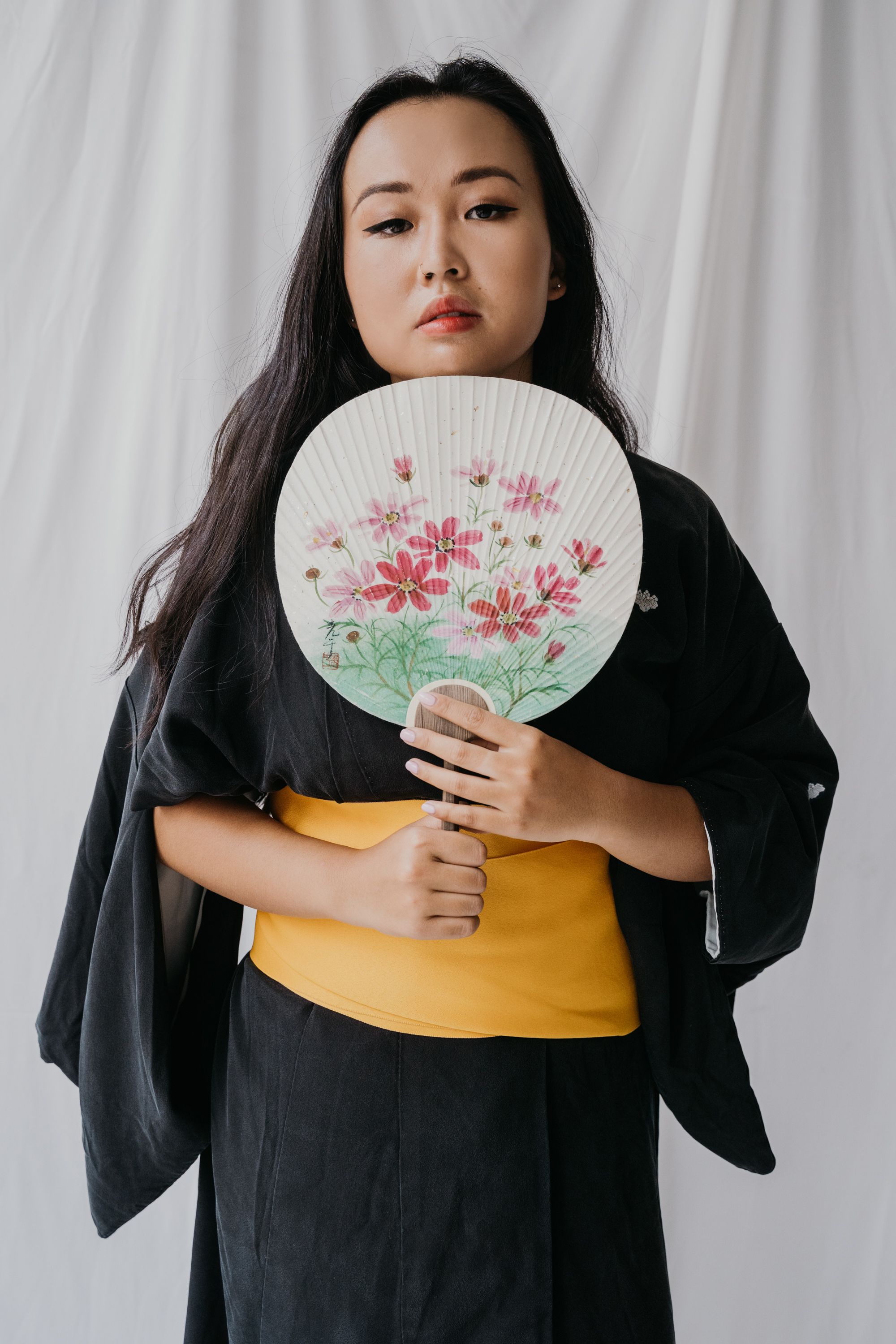一位身穿黑色和服的亚洲妇女手握一把带有花卉图案的装饰纸扇的肖像
