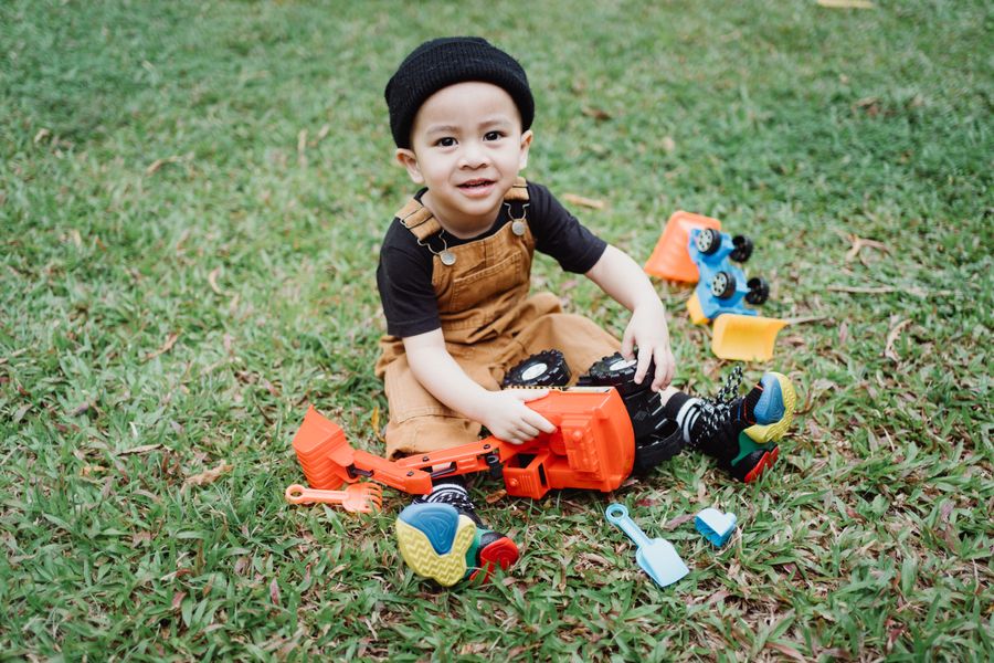 Toddler in overalls playing with toy trucks on the grass