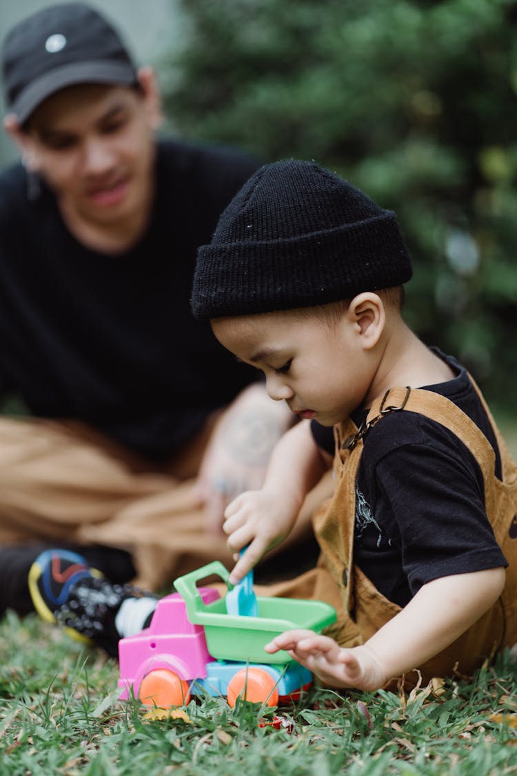 Father And Son Sitting On Grass Playing With Toys