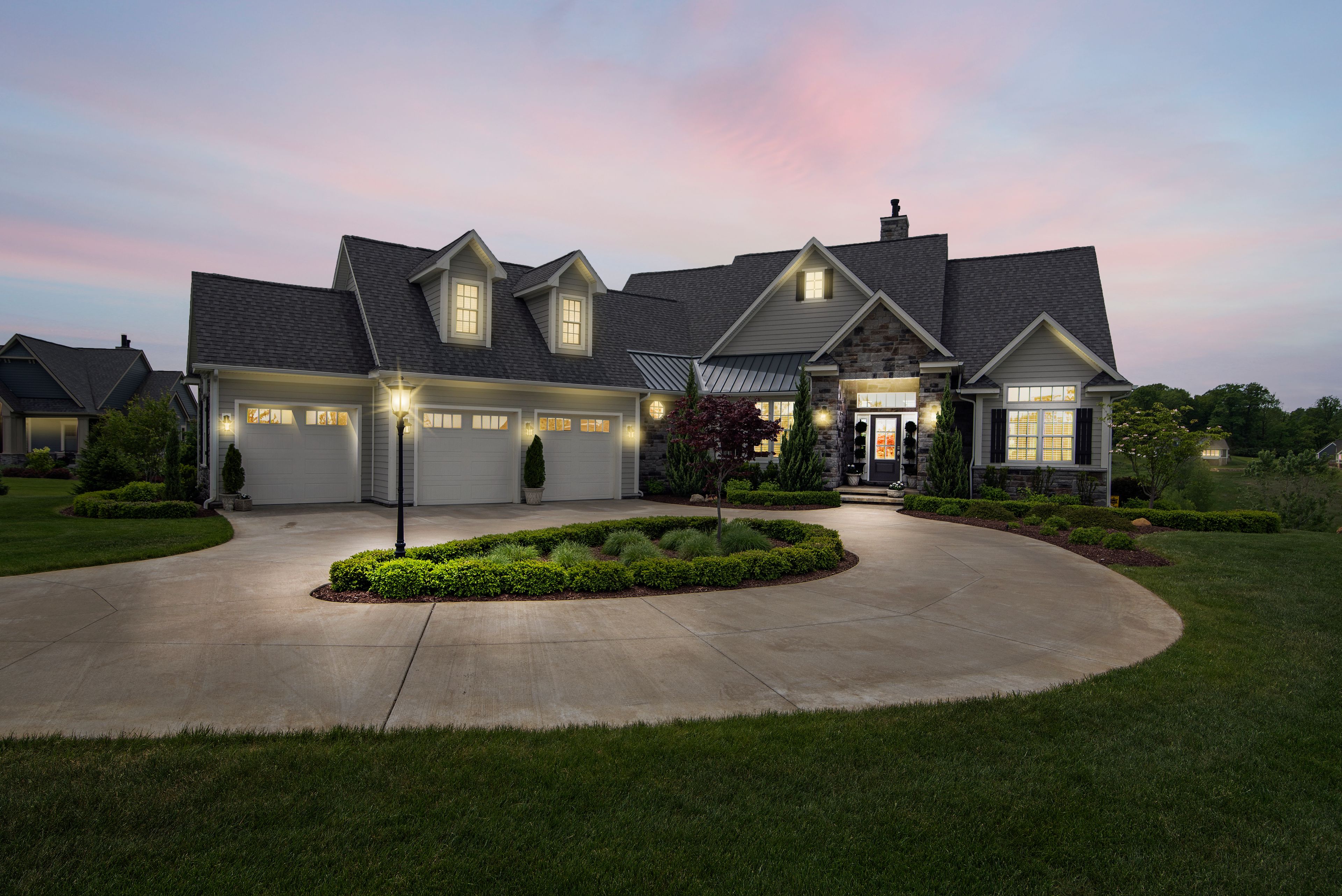 Stone and shingle family home behind a circular drive at dusk
