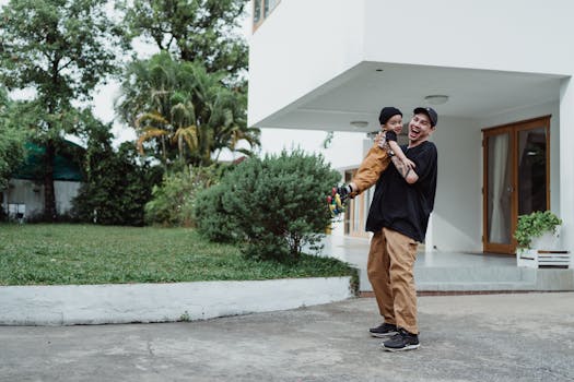A joyful father lifts his son playfully outside their modern home.