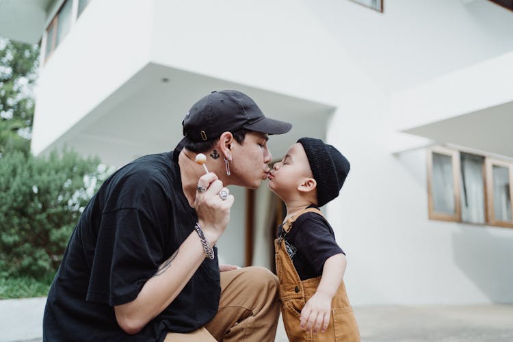 Man Kissing Son And Holding Lollipop In Front Of A House