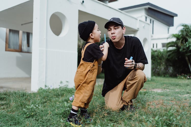 Portrait Of Man With Son Blowing Soap Bubbles In Front Of House