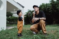 Man in Black Crew Neck T-shirt and Brown Pants Holding Baby in Orange Pants