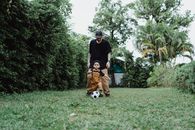 Man in Black Long Sleeve Shirt and Brown Short Coated Dog on Green Grass Field during