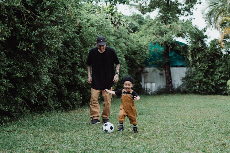 Father And Son Playing With Ball In Yard