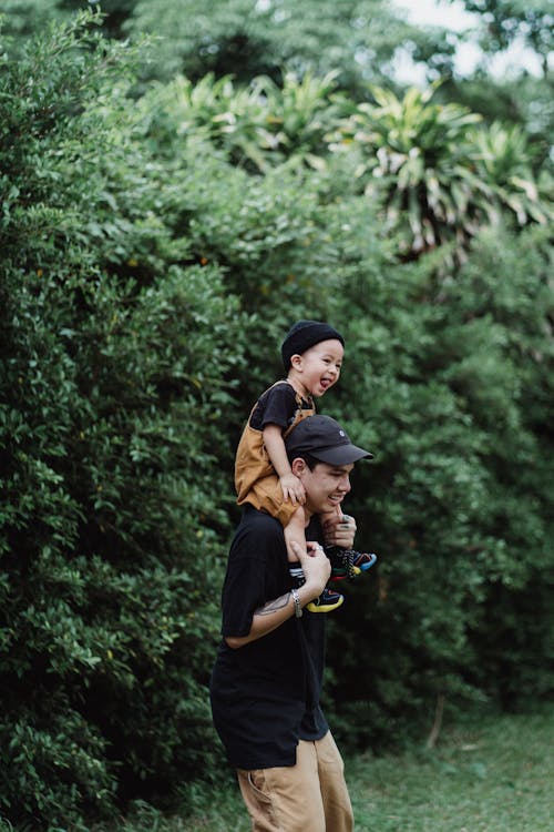 Father Carrying His Little Son on His Shoulders and Smiling