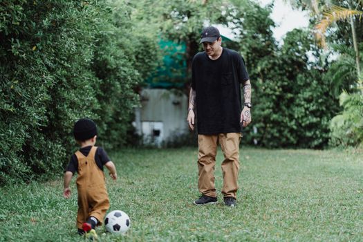 一位父亲和年幼的儿子在花园郁郁葱葱的草坪上一起踢足球