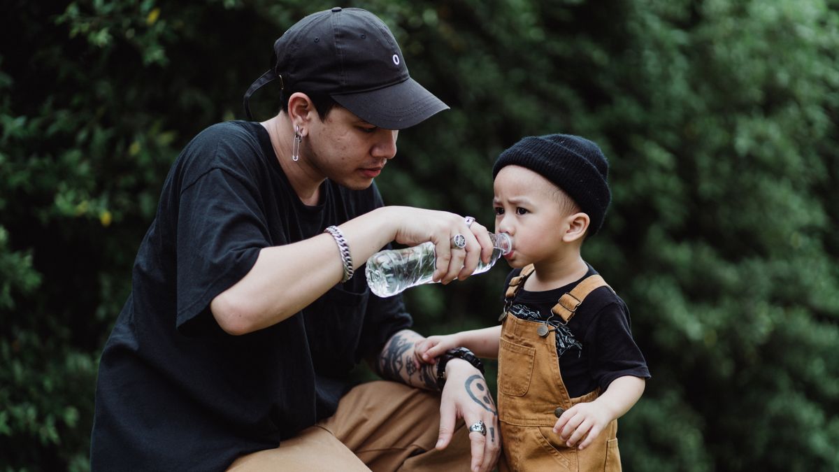 Father helping his young son drink water outside, showing signs of dehydration in kids being prevented