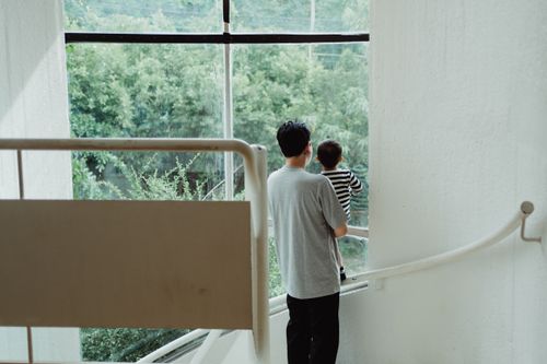 Free A man holding a child looks out a large window, standing on a staircase. Stock Photo