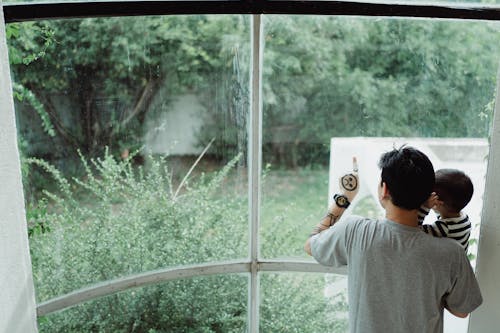 Father Carrying His Son and Pointing at Something Through the Window 