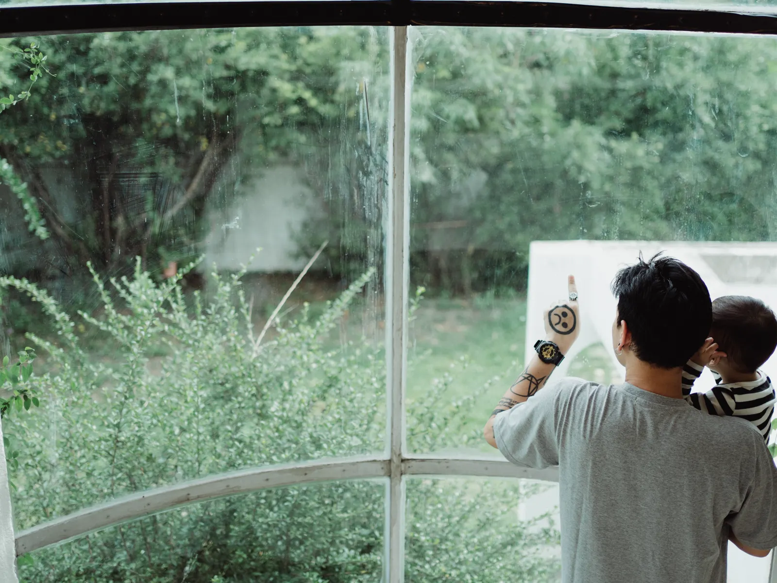 A father and young son pointing together out a window at a green garden
