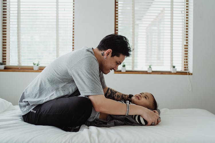 Father And Son Playing While Sitting On A Bed 