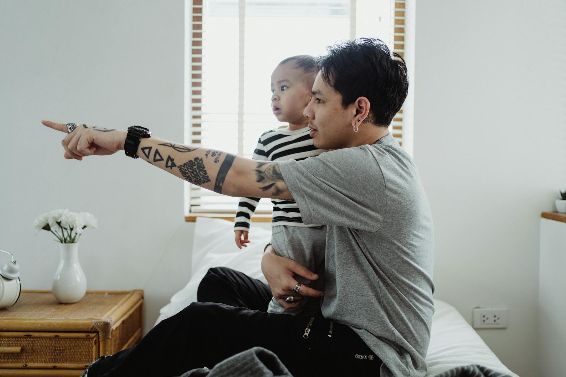 A father and son sharing a moment of togetherness and curiosity in a modern bedroom setting.