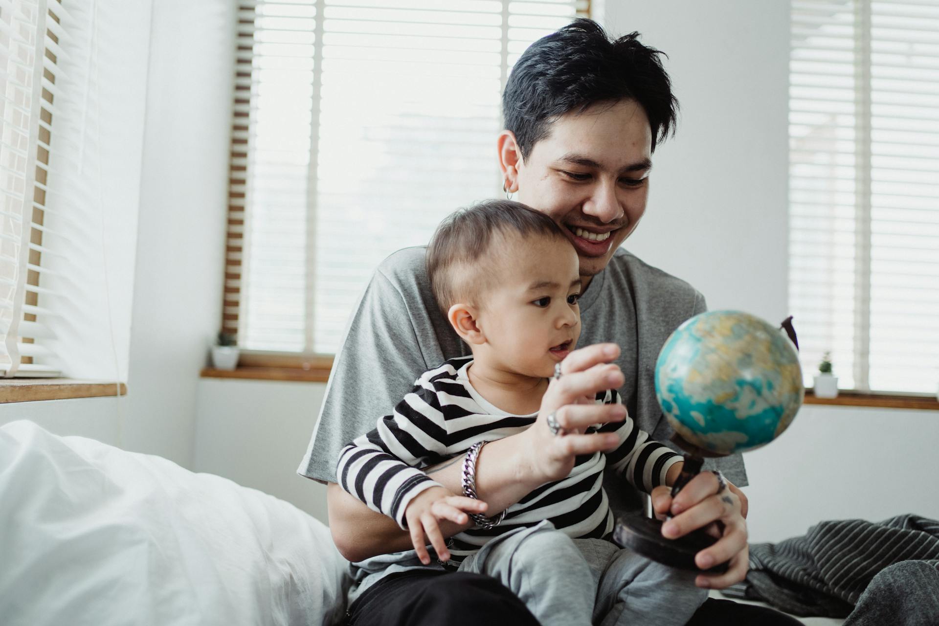 Father and son bonding over a globe in a peaceful bedroom setting. Smiling and learning together.