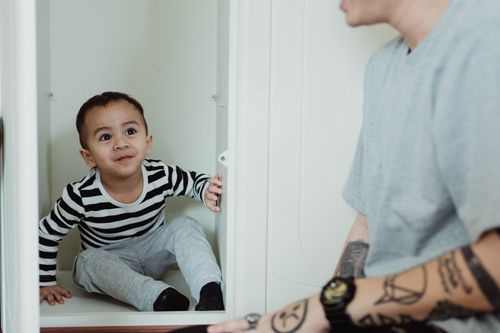 Free A happy child sitting playfully inside a cupboard, smiling with delight. Stock Photo