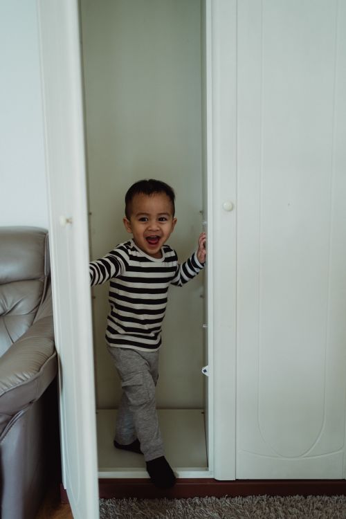 Free A joyful child in striped shirt playing inside a white wardrobe, full of laughter. Stock Photo