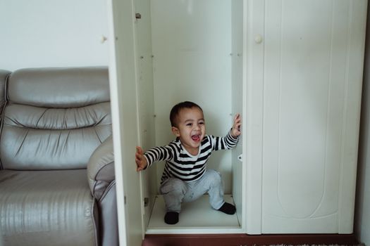 A cheerful child in striped clothing hiding in a white wardrobe, expressing excitement.