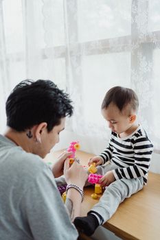 一位父亲在室内陪小儿子玩着色彩缤纷的玩具，享受着美好的亲子时光