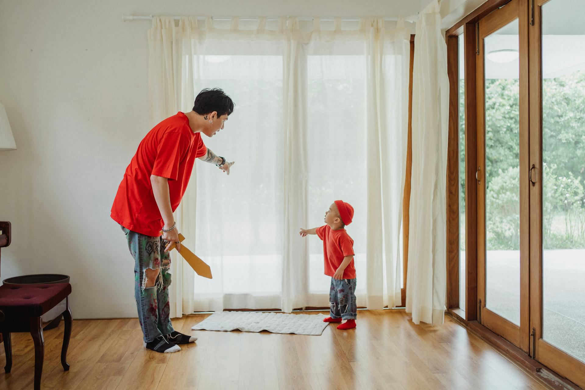 Father and son bonding indoors, playing with a toy sword in a bright living room.