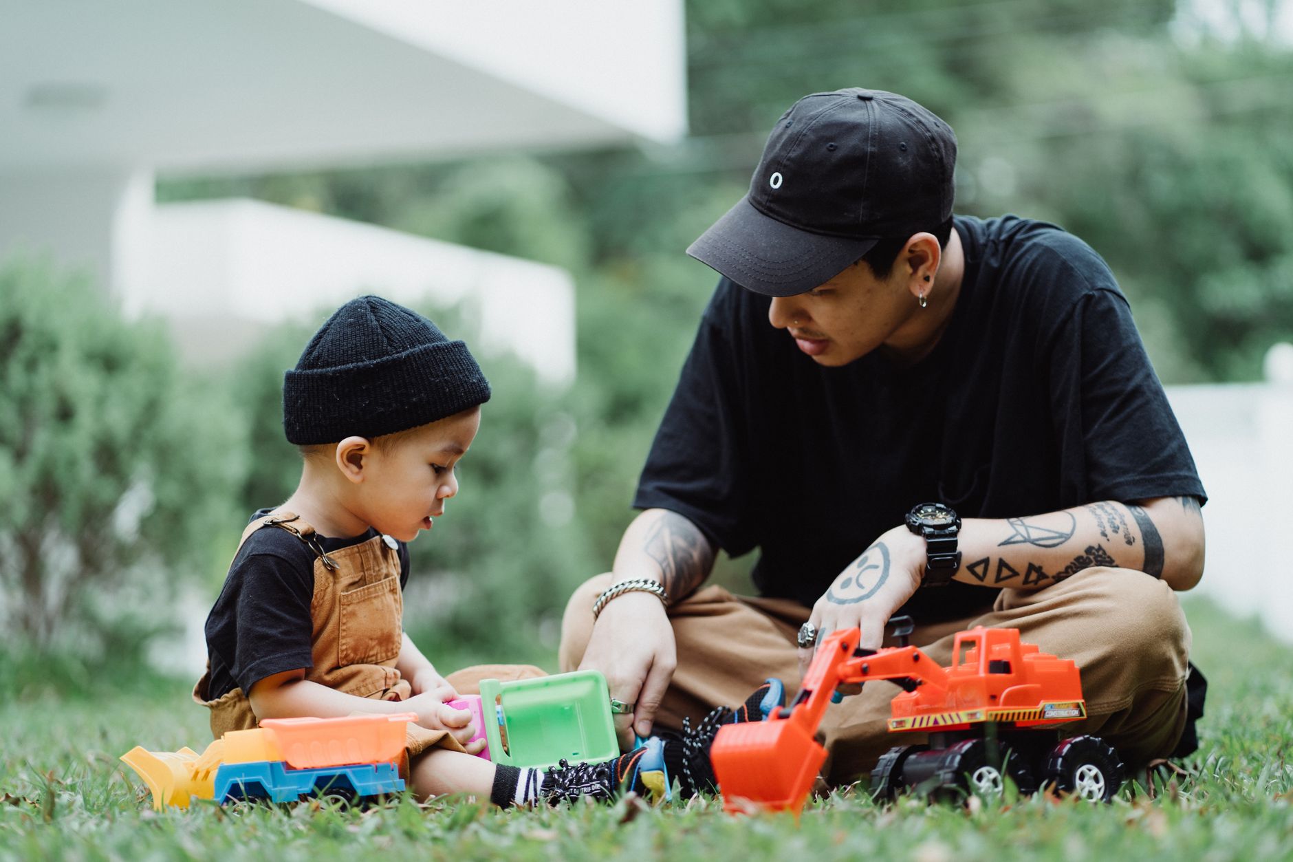 Dad and young son playing with toy cars in the backyard, ordinary time where boys watch how men act